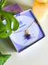 Handmade amethyst clover necklace with gold wire wrapping in aesthetic flat lay styling with candle and plant, beautifully presented in Laganna jewelry box - healing crystal jewelry crafted by Sri Lankan artisan for calm and spiritual balance