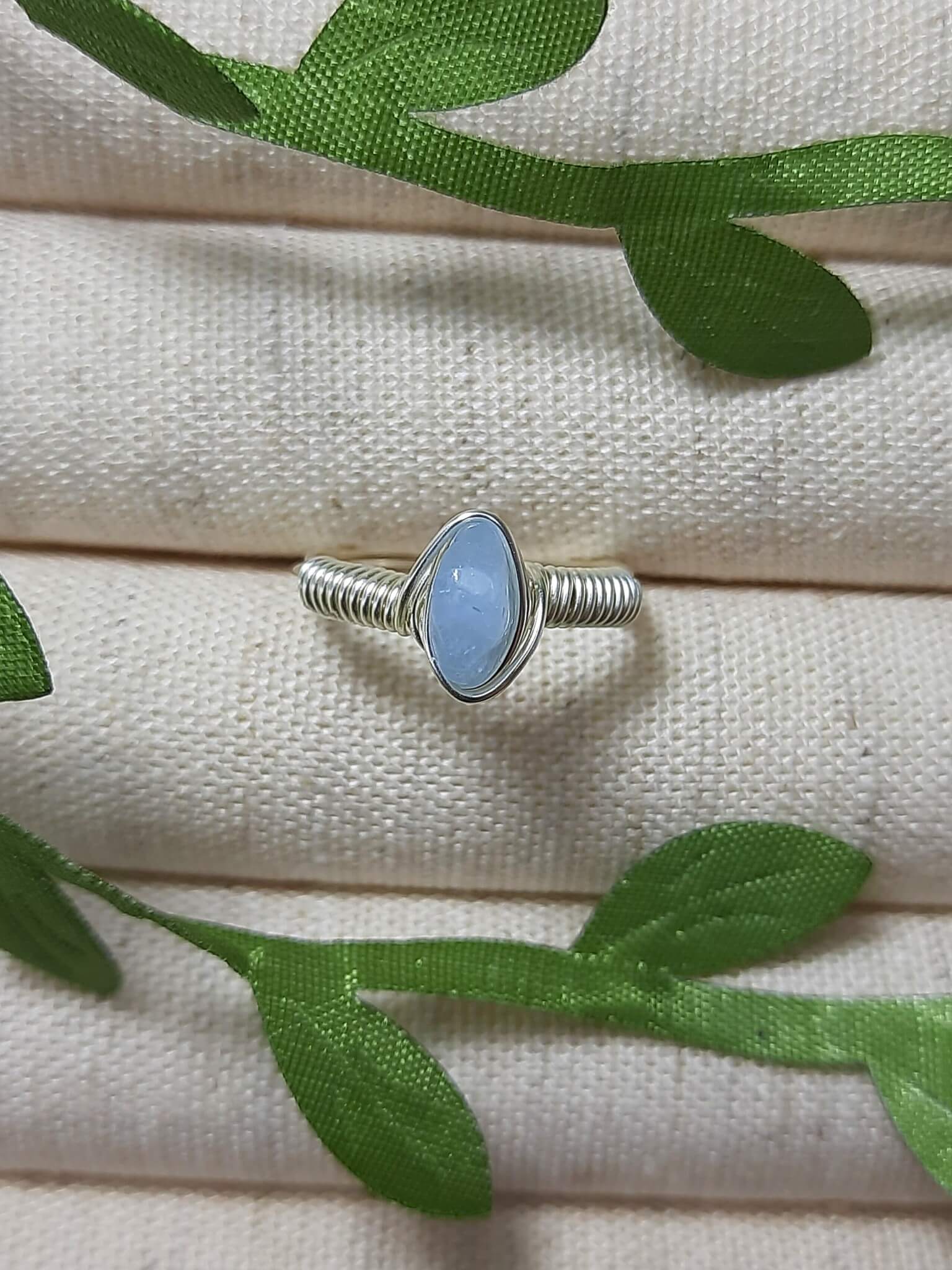 Natural aquamarine irregular stone ring in silver wire wrapped design on jewelry display showing handmade healing crystal jewelry, Sri Lankan artisan spiritual ring with raw blue gemstone perfect as boho throat chakra ring and protective amulet for communication and tranquility