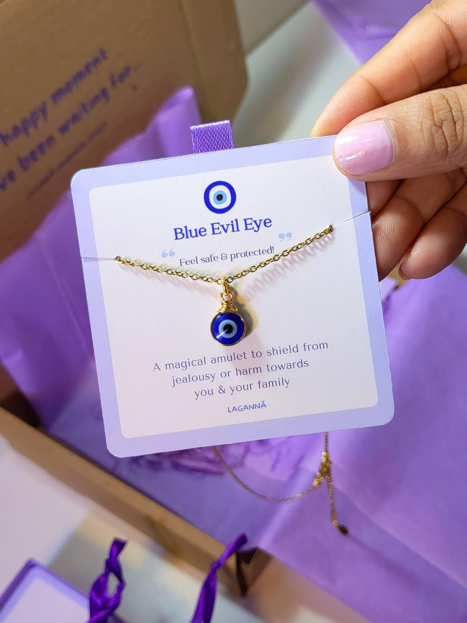 Blue evil eye necklace jewelry card held in hand showing handmade gold protection pendant packaging, Sri Lankan spiritual jewelry gift set featuring wire wrapped healing crystal necklace as evil eye talisman with elegant presentation for metaphysical jewelry lovers