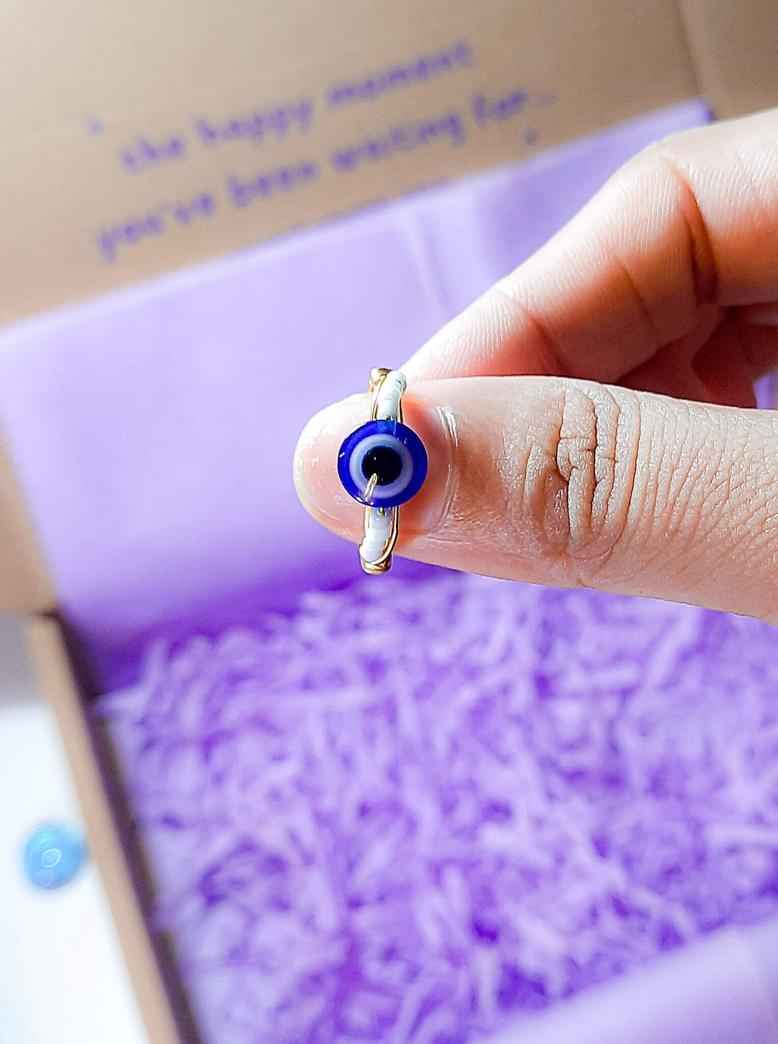 Blue evil eye seed bead ring held on hand showing gold wire wrapped design, handmade Sri Lankan protective talisman ring for warding off negative energy