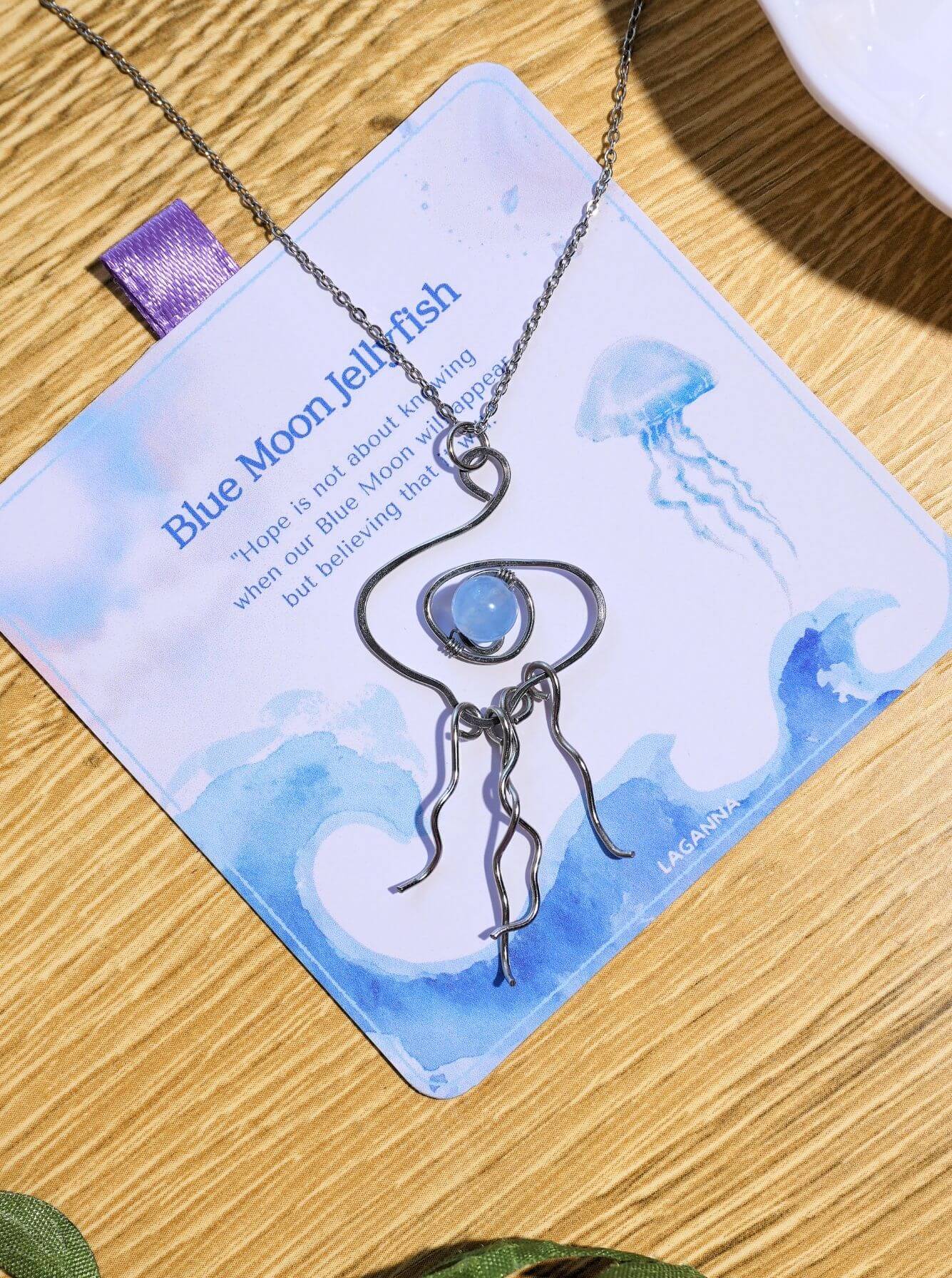 Blue Moon Jellyfish Necklace with Blue Chalcedony displayed on Laganna gift box with crystals and greenery lifestyle styling handmade Sri Lanka stainless steel wire jellyfish pendant meaningful gift healing crystal jewelry