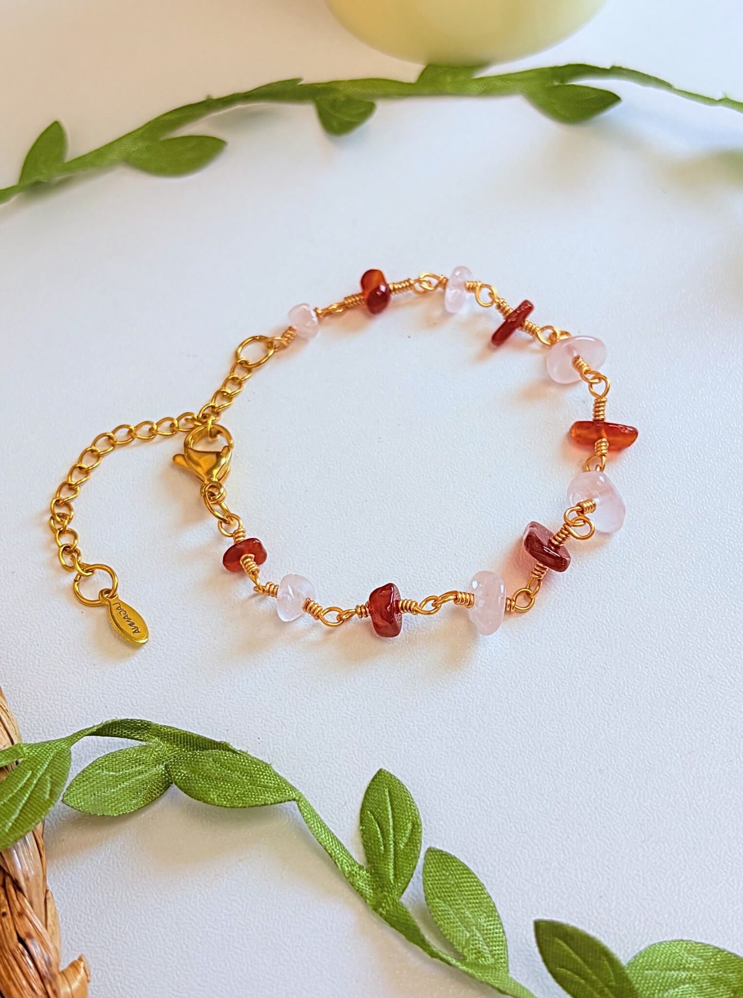 Chinese Red Lantern Bracelet carnelian and rose quartz chip stones gold wire wrapped overhead flat lay with green leaves and rattan prop, handmade healing crystal bracelet Sri Lanka – good fortune motivation love Laganna