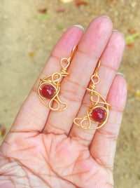 Crescent moon dangle earrings with carnelian held on hand, handmade Sri Lankan gold wire wrapped celestial earrings for sacral chakra and creative energy