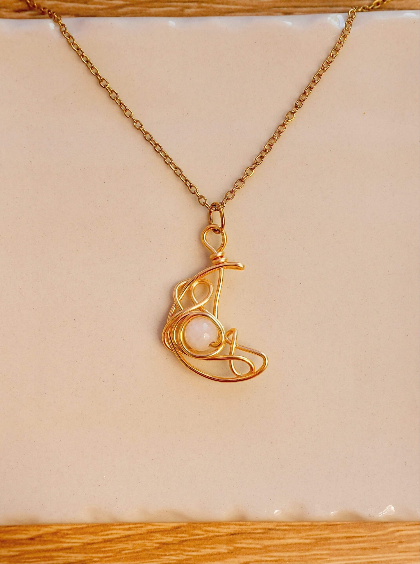 Crescent Moon Necklace Moonstone gold wire crescent pendant resting on white ceramic surface artistic flat lay, handmade healing crystal necklace Sri Lanka Laganna