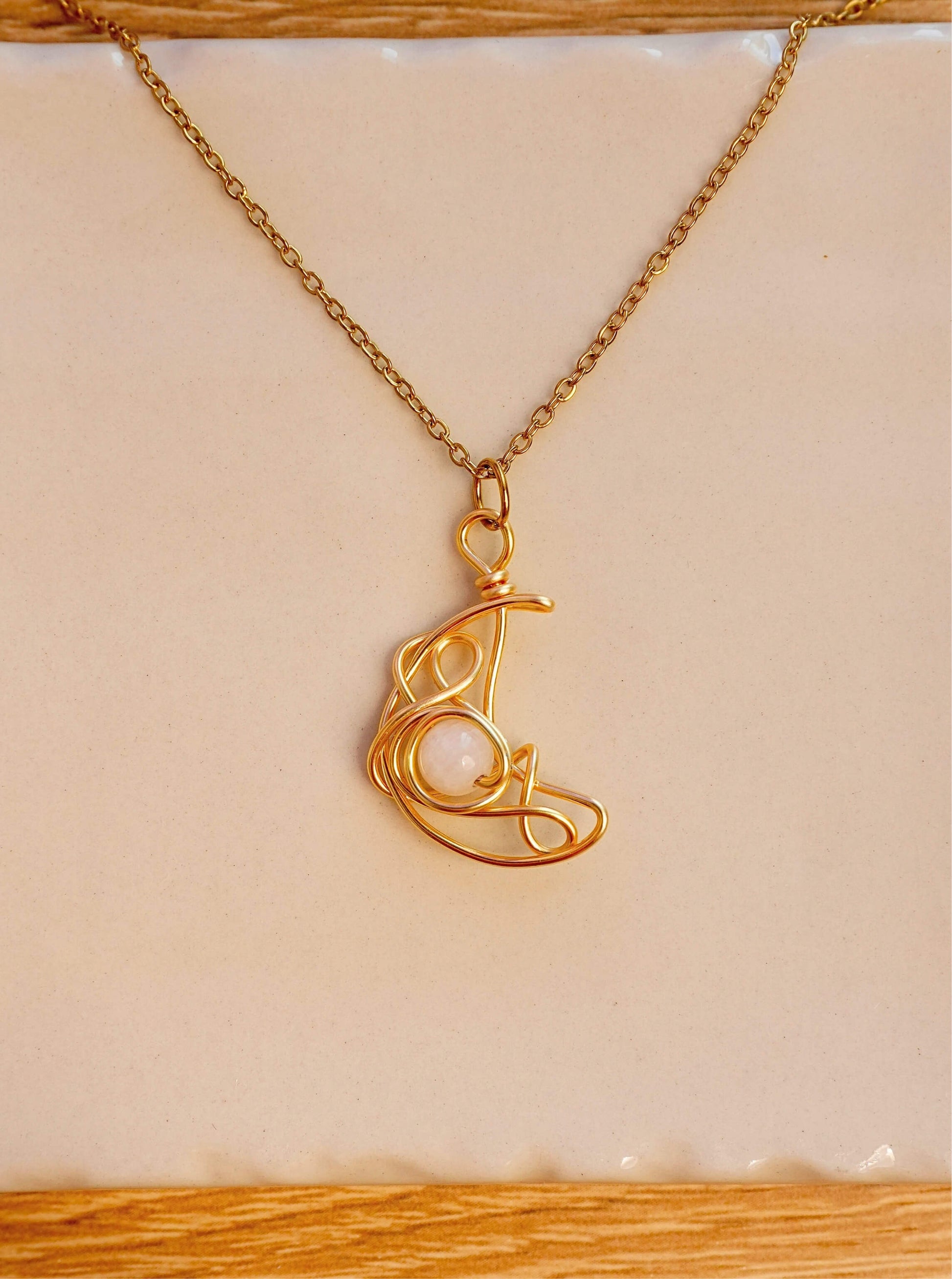 Crescent Moon Necklace Moonstone gold wire crescent pendant resting on white ceramic surface artistic flat lay, handmade healing crystal necklace Sri Lanka Laganna
