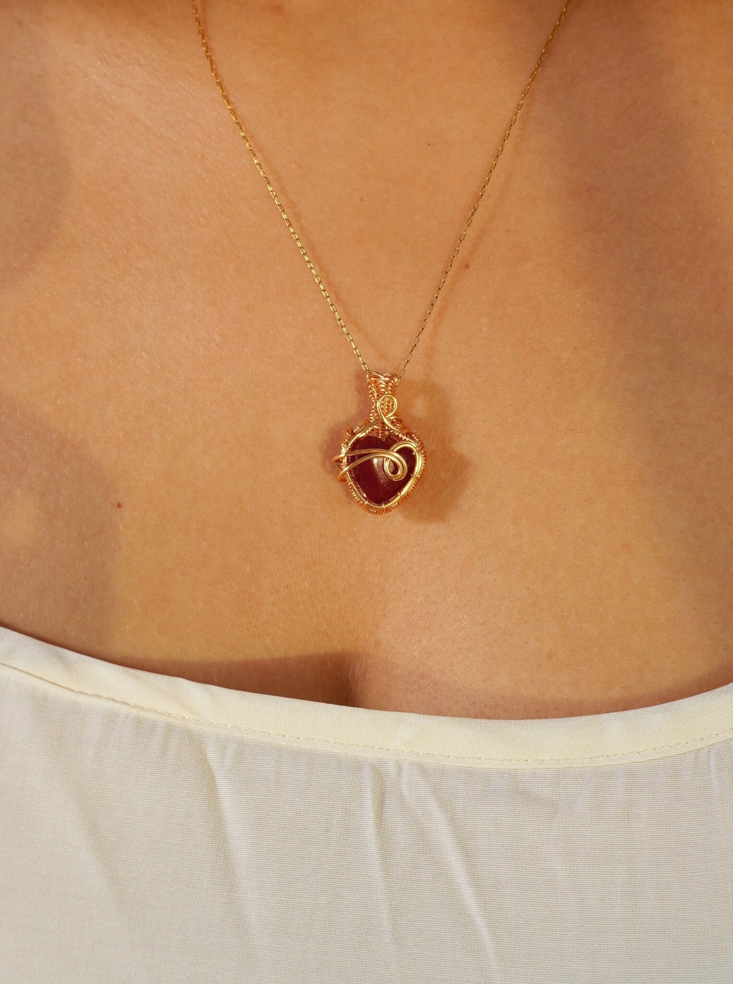 Close-up of Red Chalcedony heart pendant necklace with intricate gold wire wrapping worn on model – handmade healing crystal jewelry from Sri Lanka, warm tones love jewelry
