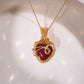 Red Chalcedony heart-shaped crystal pendant with detailed gold wire wrap on delicate chain, styled on white ceramic dish – artisan handcrafted necklace by Laganna Sri Lanka
