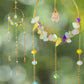 Handmade crystal blessing suncatcher featuring wire-wrapped rose quartz, amethyst, citrine, aquamarine, fluorite gemstones and rainbow glass beads on gold brass hoop catching natural light - bohemian healing crystal home decor from Sri Lanka for positive energy