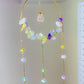 Close-up of artisan crystal blessing suncatcher with wire-wrapped rose quartz pendant, moon charm, amethyst, citrine, aquamarine, fluorite chips and iridescent glass beads on golden brass frame - handmade spiritual window decor from Sri Lanka for abundance and peace