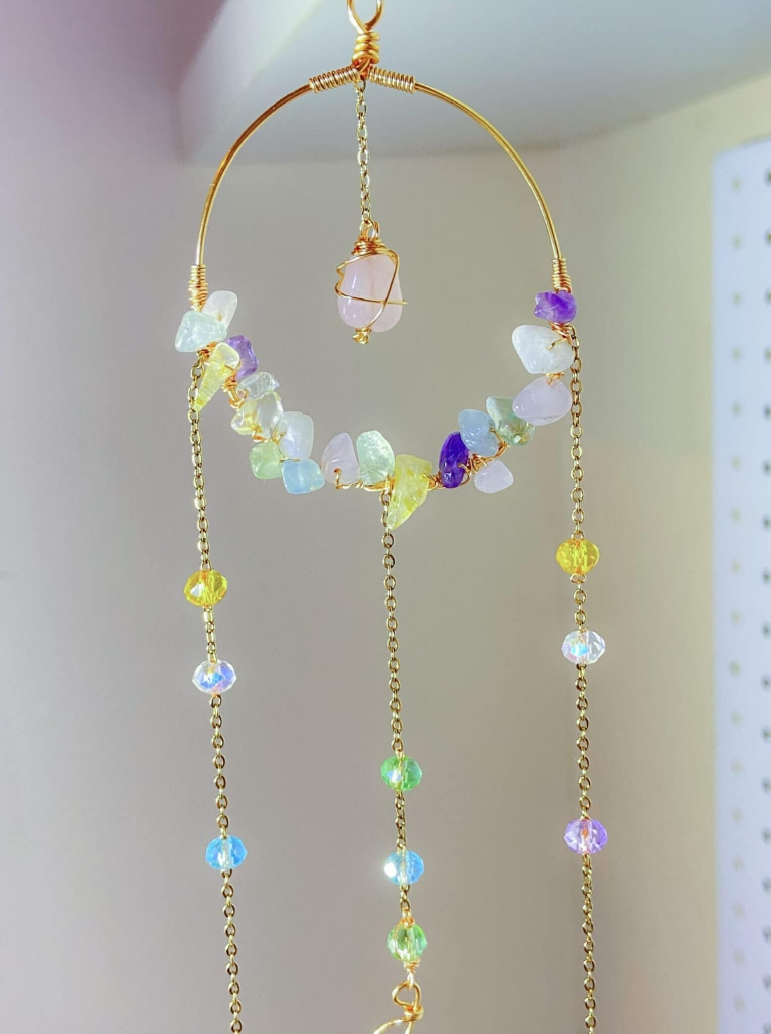 Close-up of artisan crystal blessing suncatcher with wire-wrapped rose quartz pendant, moon charm, amethyst, citrine, aquamarine, fluorite chips and iridescent glass beads on golden brass frame - handmade spiritual window decor from Sri Lanka for abundance and peace