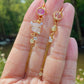 Mismatched dangle earrings with rose quartz and citrine held on hand with nature background, handmade Sri Lankan crystal planet earrings for heart chakra and prosperity