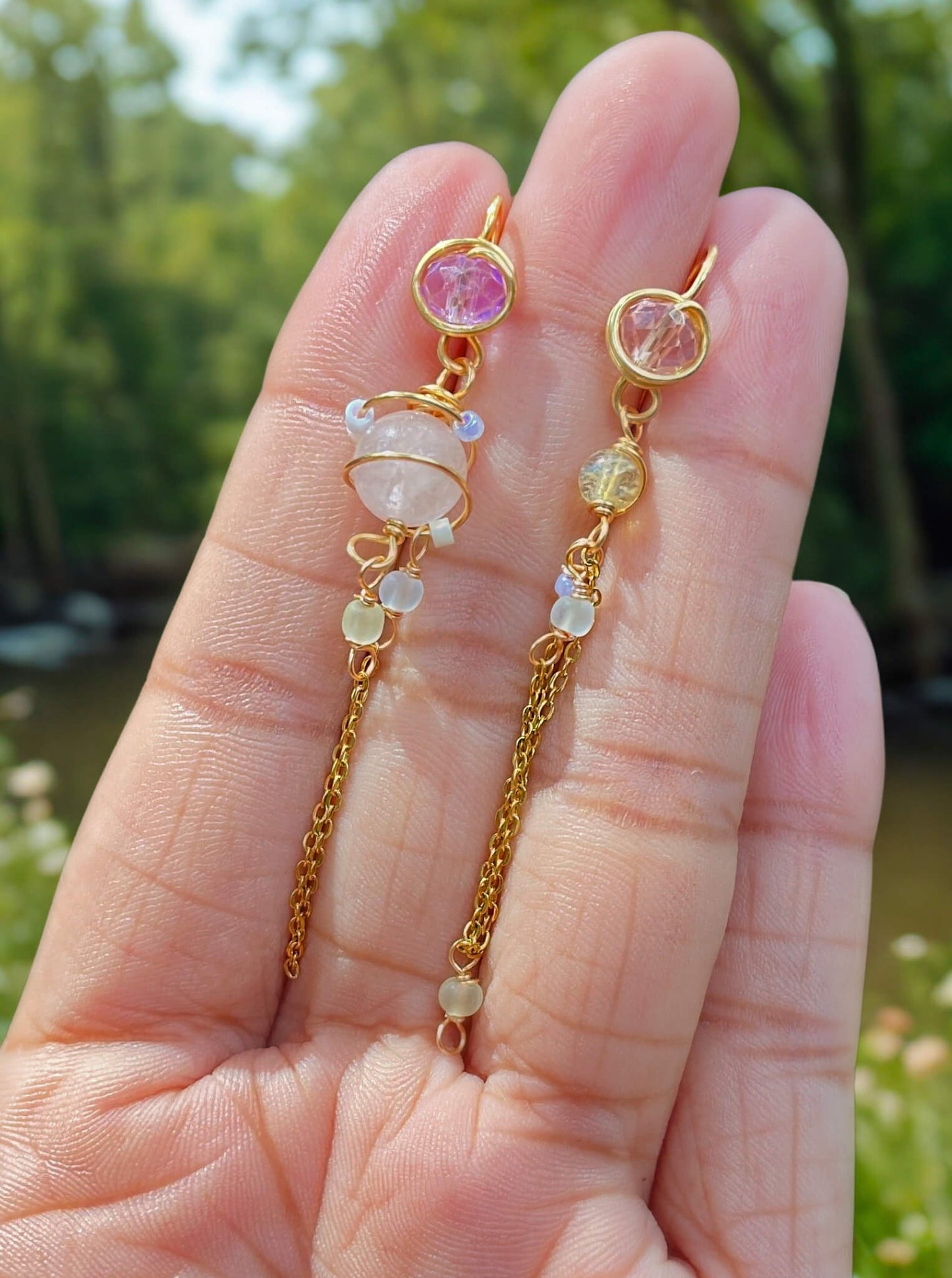 Mismatched dangle earrings with rose quartz and citrine held on hand with nature background, handmade Sri Lankan crystal planet earrings for heart chakra and prosperity