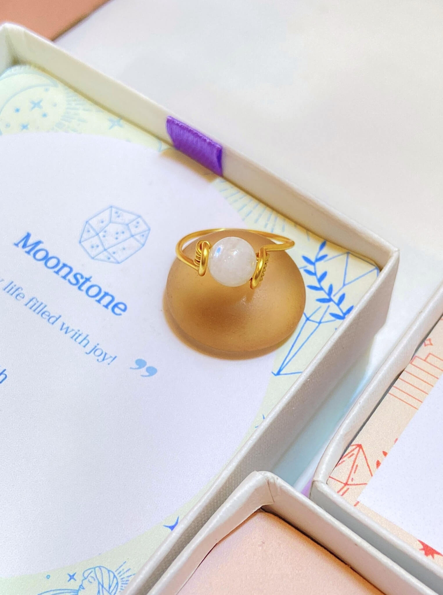 Dainty round moonstone ring jewelry box closeup showing iridescent glow, handmade Sri Lankan gold wire wrapped healing crystal ring for feminine energy
