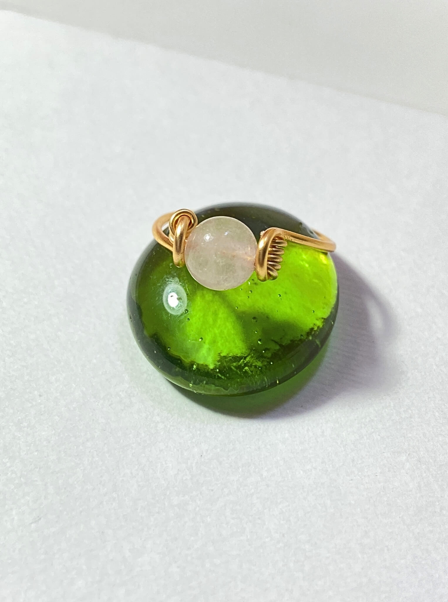 Dainty round rose quartz ring light background closeup showing gold wire wrapped design, handmade Sri Lankan healing crystal ring for emotional balance