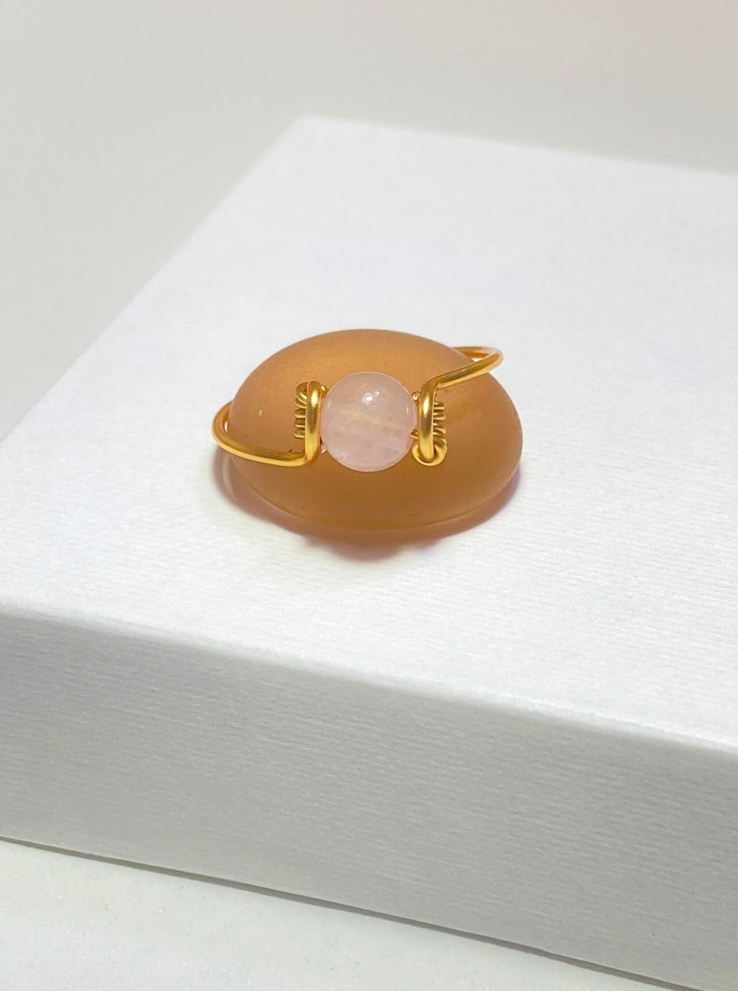 Dainty round rose quartz ring in gold wire wrap on light background, handmade Sri Lankan healing crystal ring for heart chakra and compassion