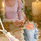 Pink top with puffed sleeves and a decorative frame, next to a blue corset and french palace column necklace on a soft background.