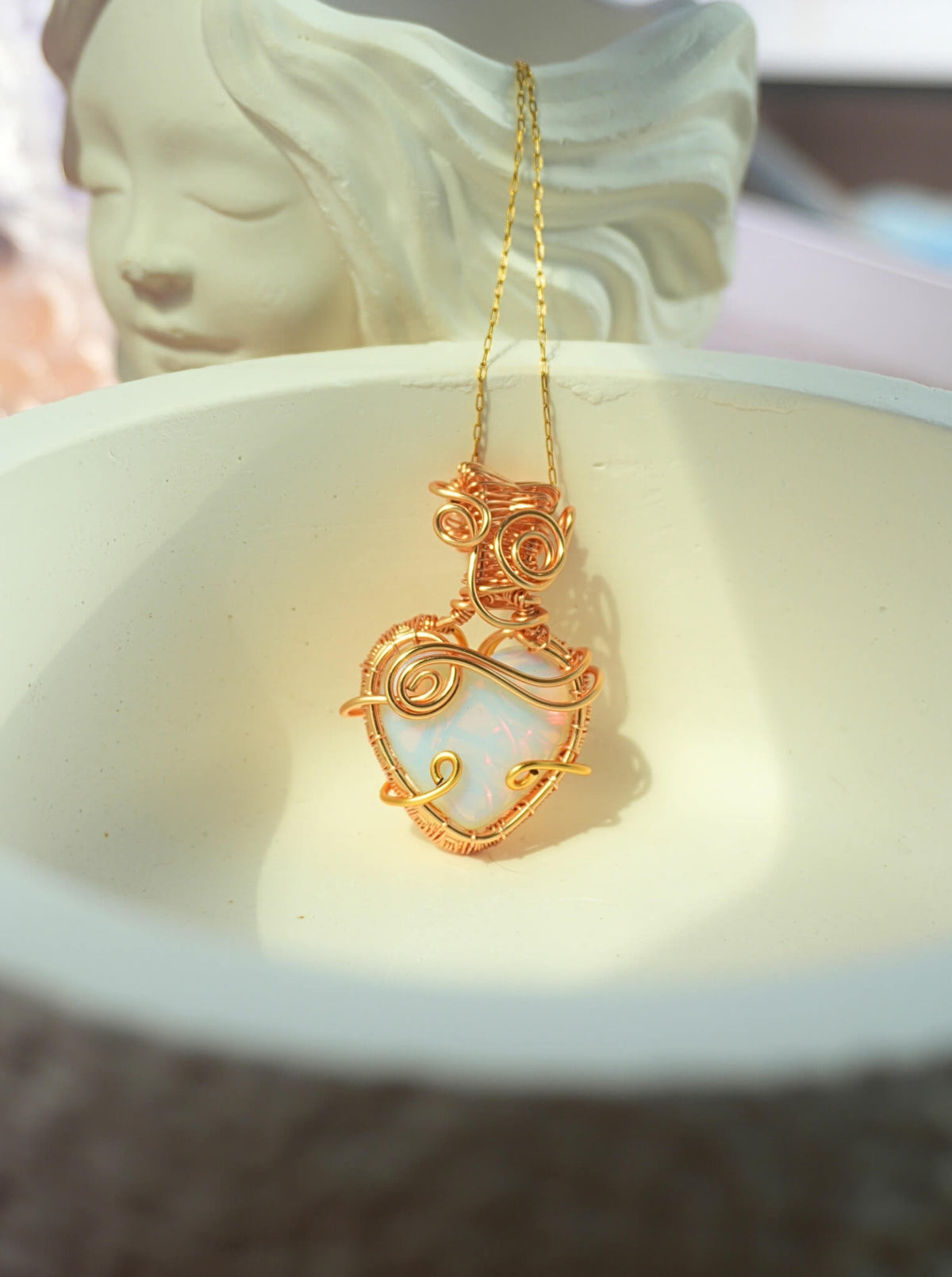 Opalite heart-shaped crystal pendant with detailed gold wire wrap on delicate chain, styled on white surface – handmade necklace by Laganna Sri Lanka
