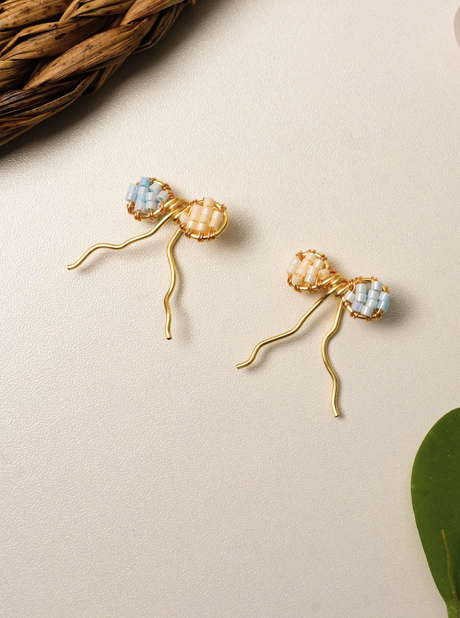 Handmade Japanese Miyuki Delica glass bead bow earrings in soft pastel peach and blue tones, lightweight wire-wrapped artisan jewelry Sri Lanka, dainty bow earrings for women, feminine handcrafted accessories by Laganna