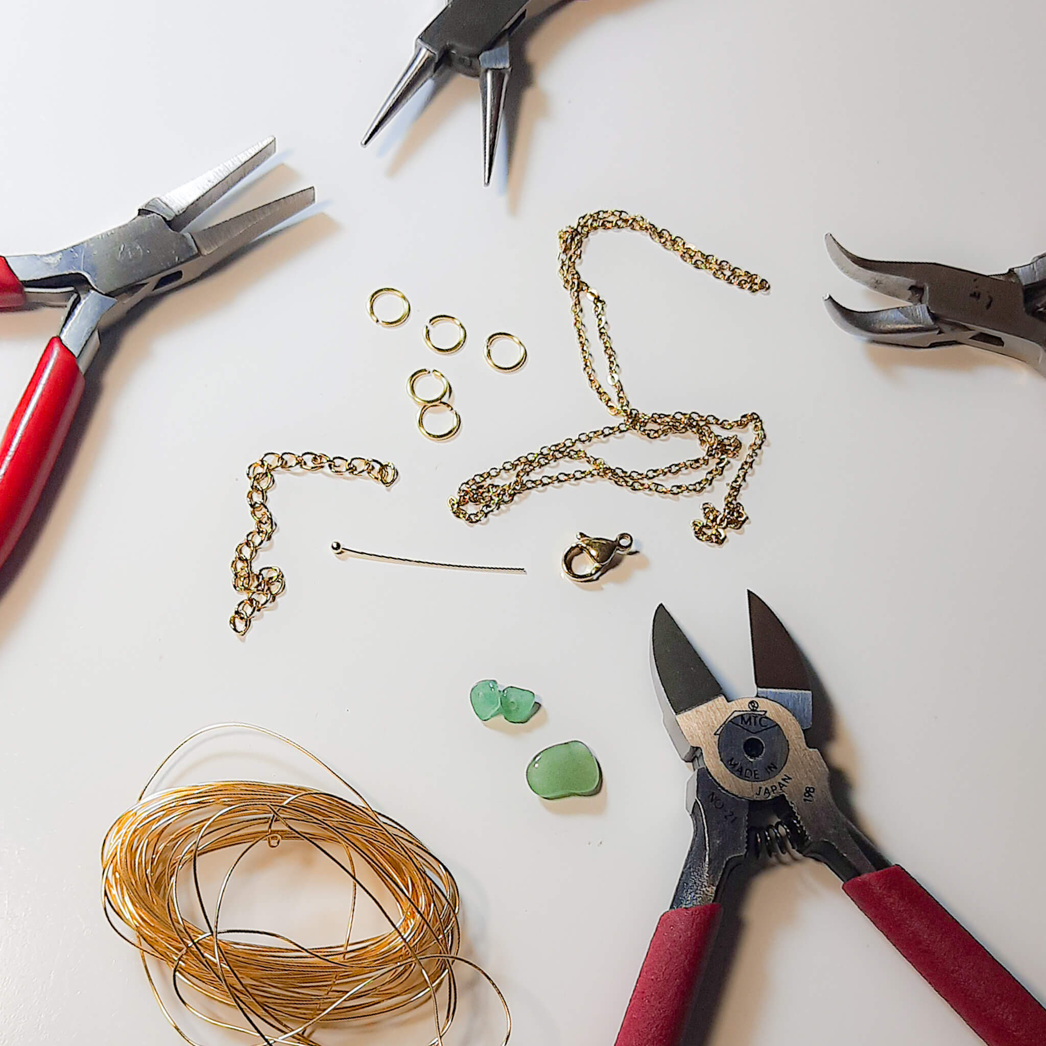 Laganna jewelry making workshop featuring professional wire wrapping tools, gold chains, jump rings, and green gemstones with precision pliers - artisan jewelry crafting process and handmade techniques in Sri Lanka 