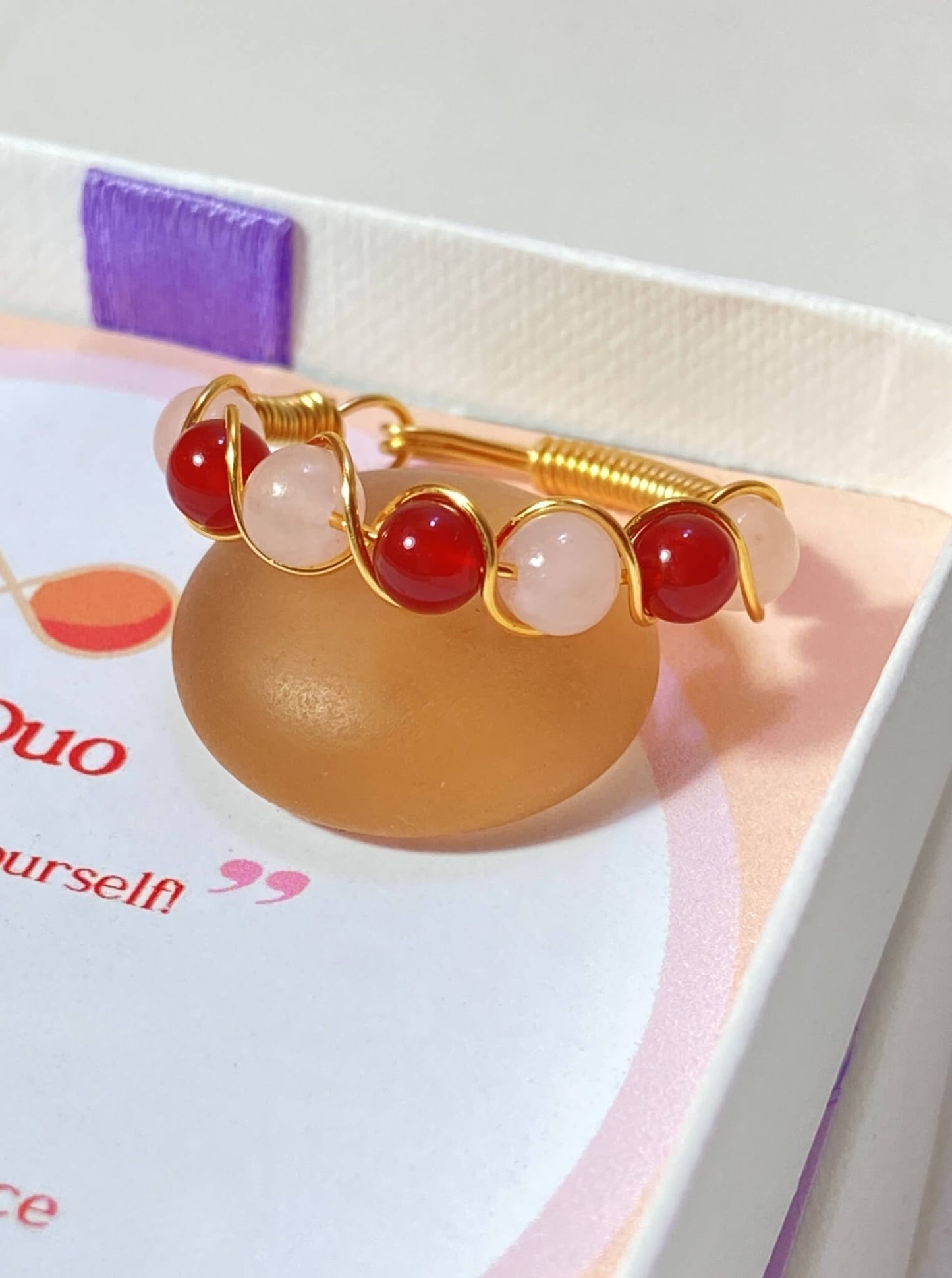 Love Duo braided ring with rose quartz and carnelian jewelry box closeup, handmade Sri Lankan gold wire wrapped dual crystal ring for love and confidence