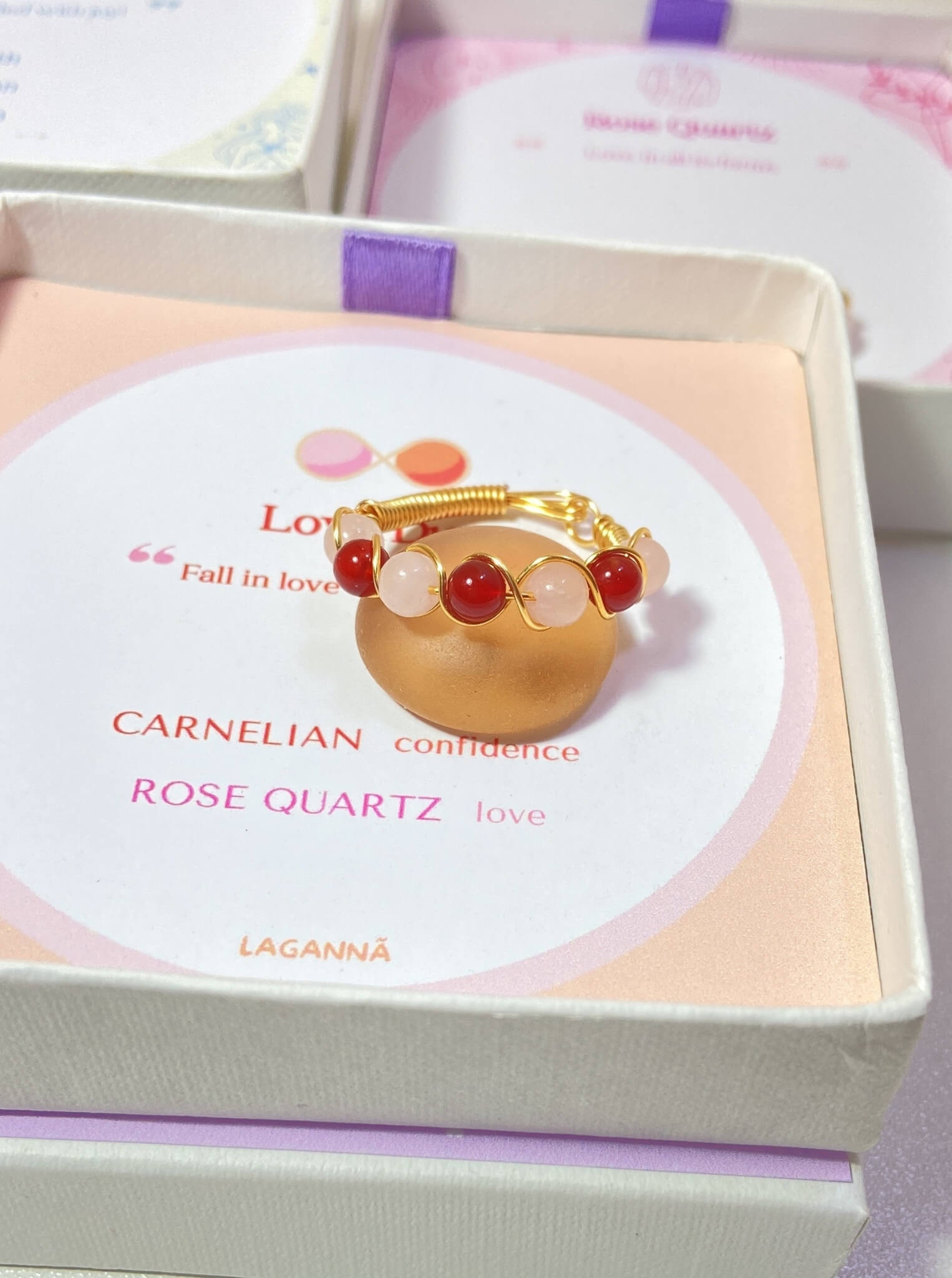 Love Duo braided ring with rose quartz and carnelian in jewelry box, handmade Sri Lankan gold wire wrapped dual crystal ring for emotional balance and motivation