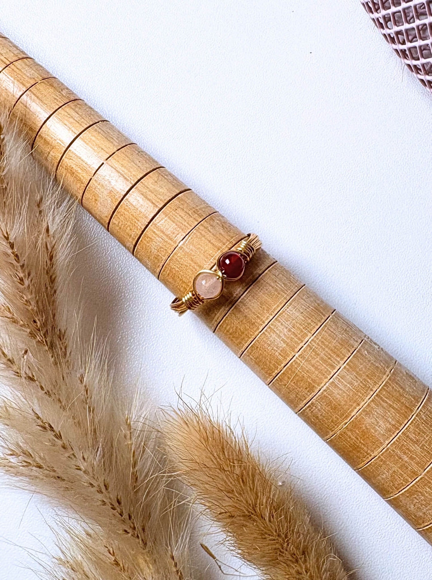 Love Duo Ring rose quartz and carnelian gold wire wrapped resting on bamboo prop with pampas grass flat lay, handmade healing crystal ring Sri Lanka – love creativity emotional balance Laganna
