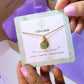 Olive jade square stone necklace jewelry card held in hand showing handmade gold wire wrapped healing crystal gift set, Sri Lankan artisan heart chakra pendant featuring natural square green gemstone perfect as abundance jewelry gift for prosperity and tranquility with elegant presentation