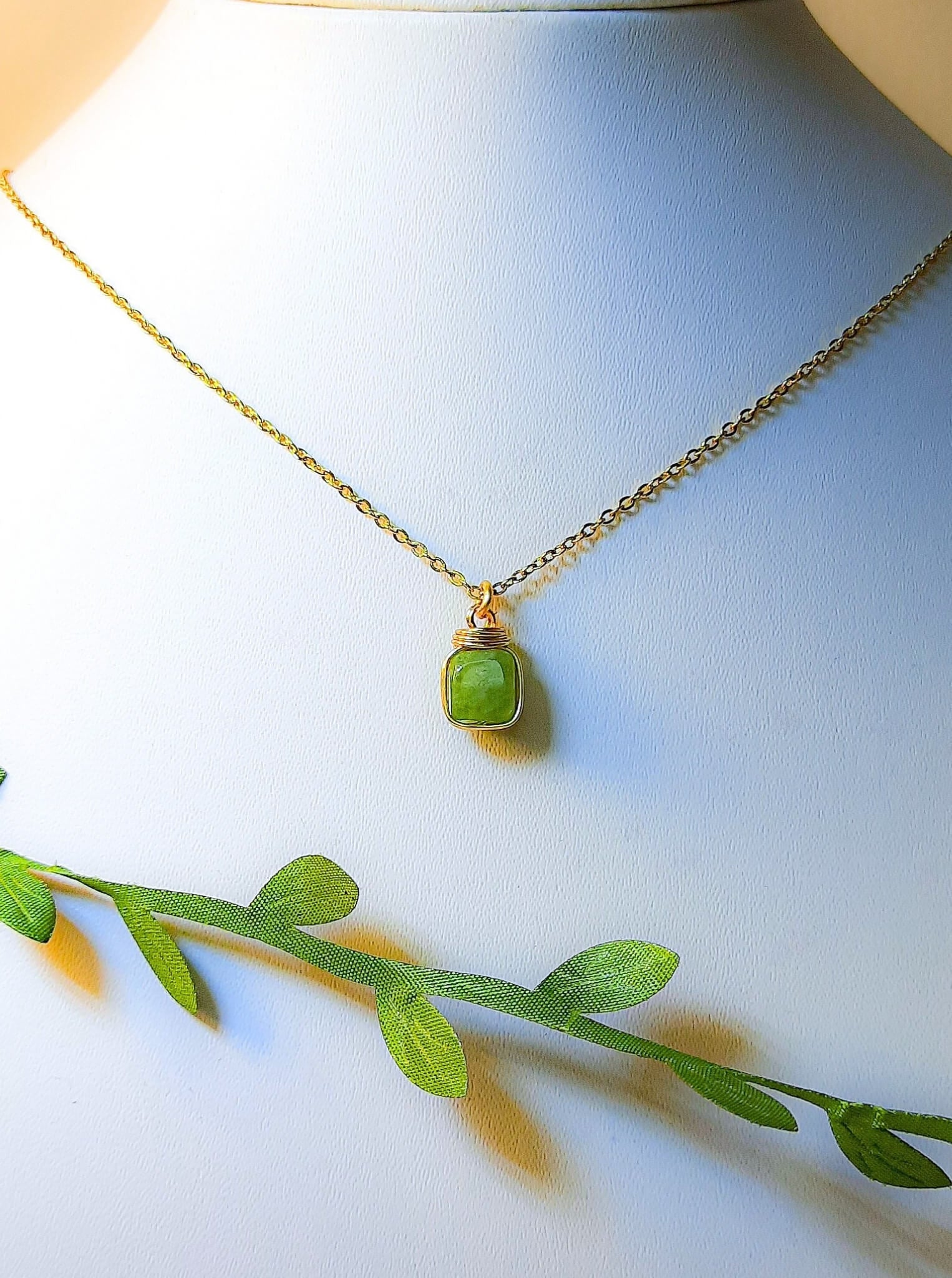 Natural olive jade square stone necklace on jewelry display showing handmade gold wire wrapped healing crystal jewelry, Sri Lankan artisan heart chakra pendant featuring geometric green gemstone perfect as boho abundance necklace and prosperity amulet for meditation and spiritual growth