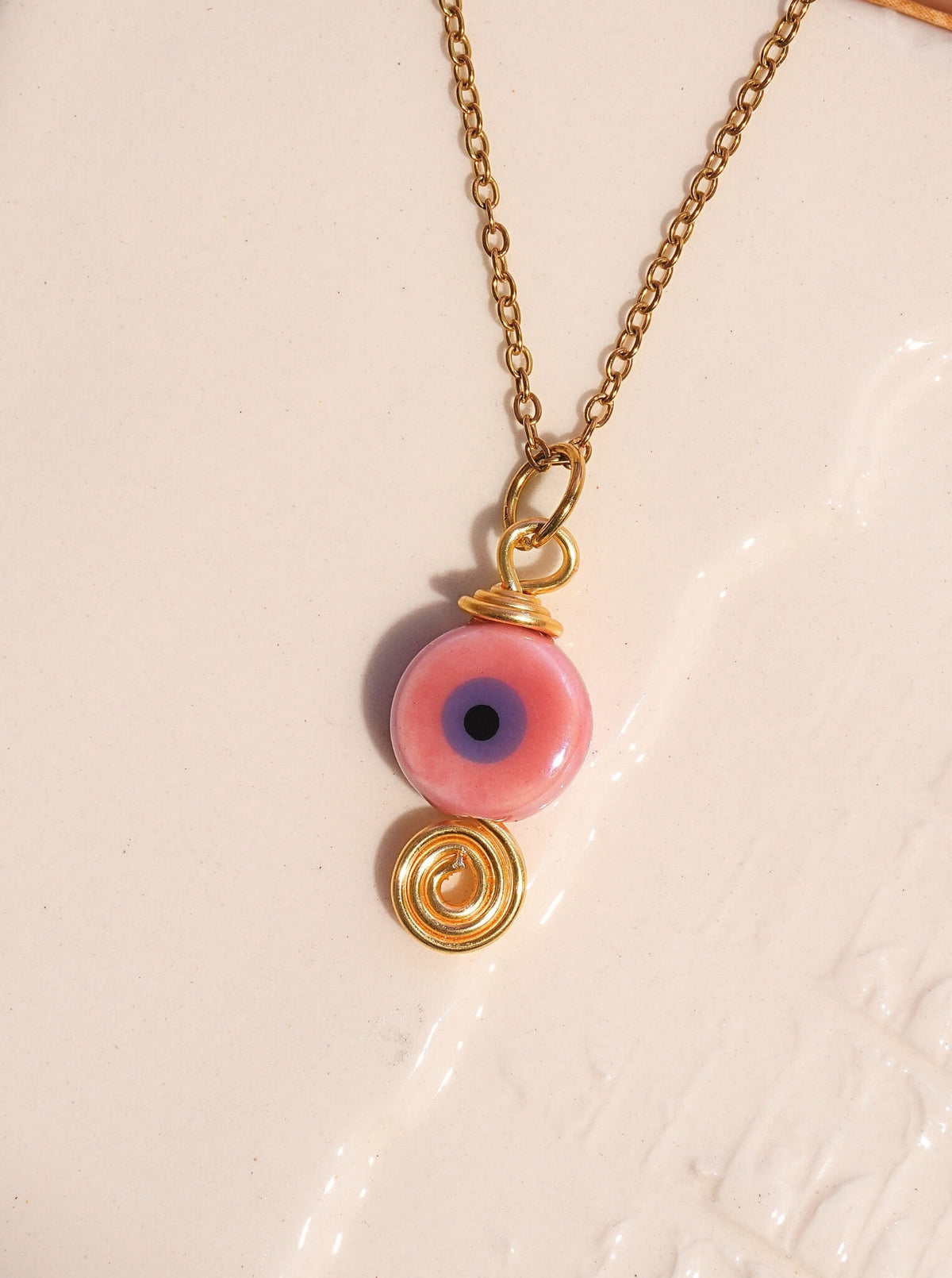 Handmade pink evil eye protection necklace in gold wire wrapped design featuring ceramic evil eye bead and spiral charm, Sri Lankan artisan spiritual jewelry crafted as self-love talisman and protective amulet for women seeking love energy and emotional healing
