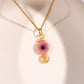 Gold pink evil eye protection necklace with ceramic bead and spiral charm on white display, handmade Sri Lankan spiritual jewelry featuring wire wrapped evil eye pendant as self-love talisman and compassion amulet for women seeking emotional balance and heart healing
