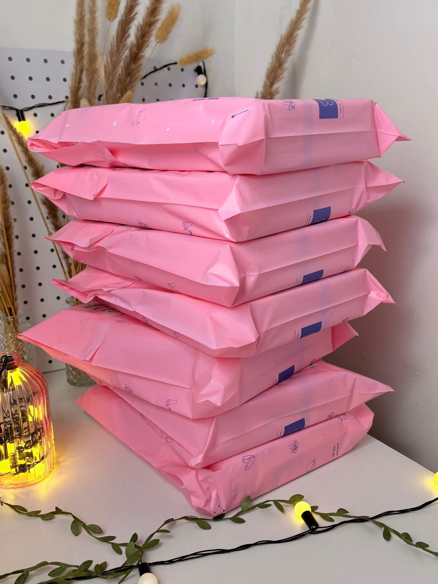 Stack of laganna jewelry pink packages on a white surface with decorative lights and plants.