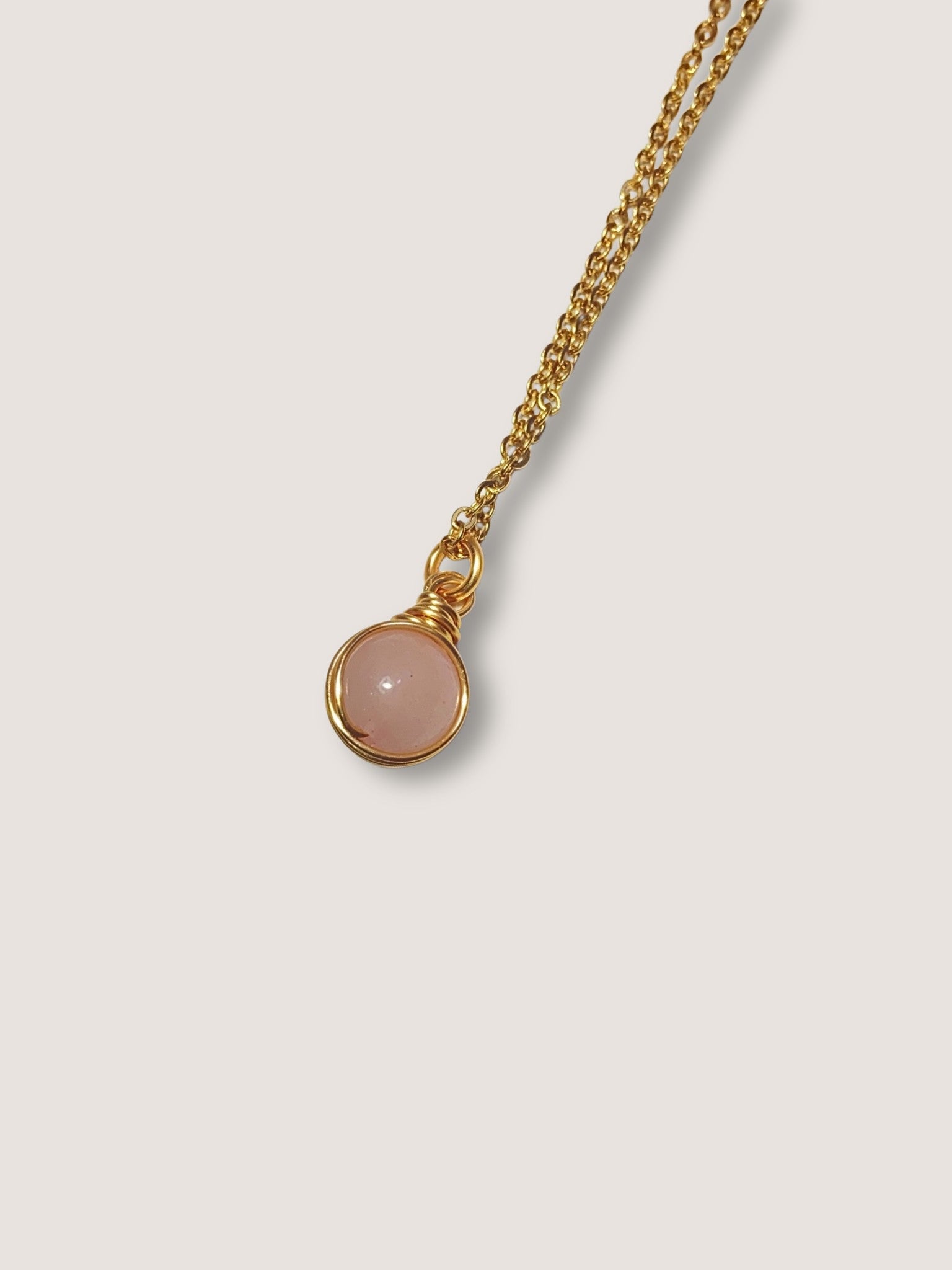 Elegant rose quartz round stone pendant necklace on white background, showcasing minimalist gold wire wrapped design - handmade healing crystal jewelry from Sri Lanka for love energy and emotional wellness