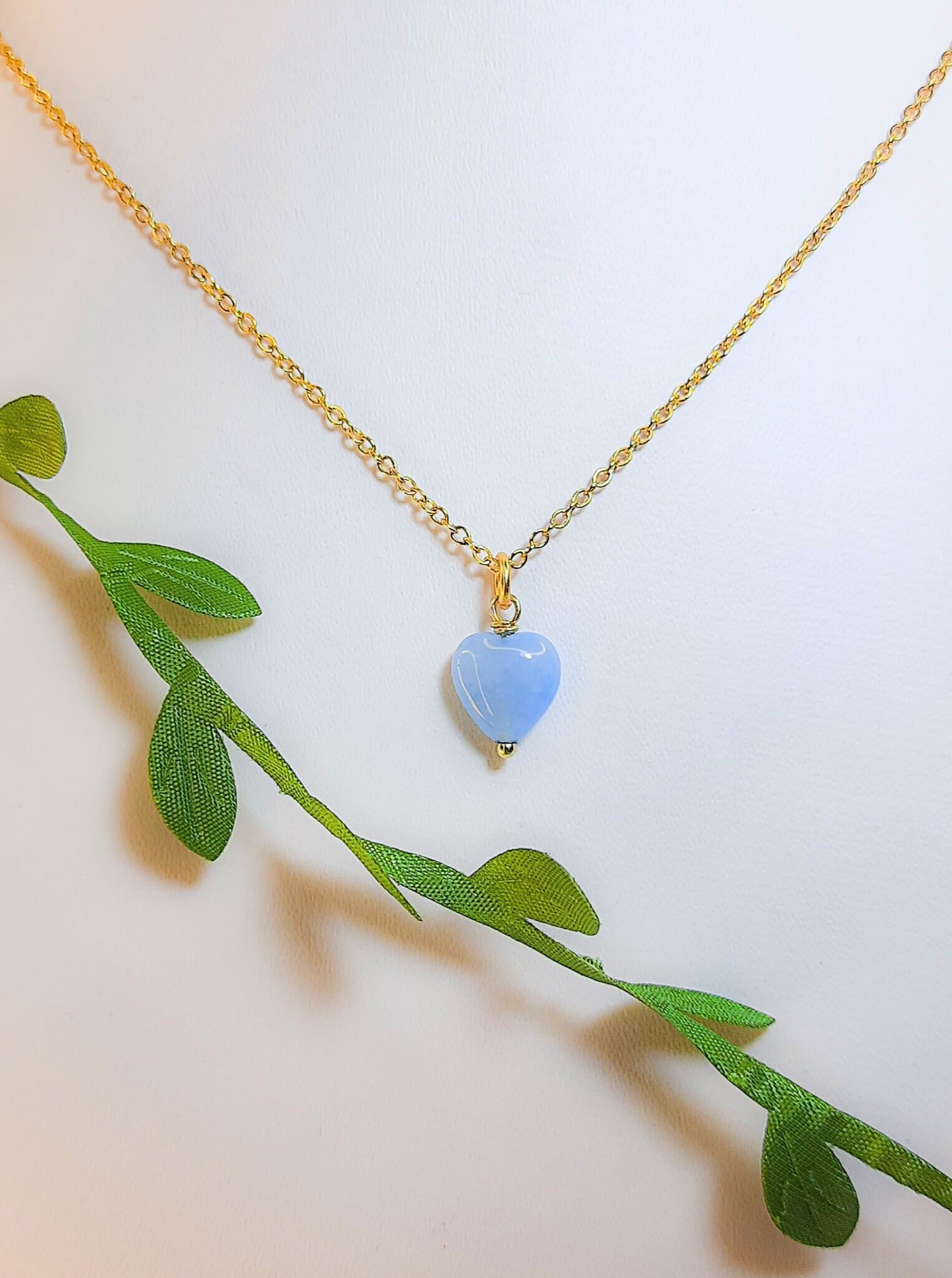 Handmade sweet heart blue chalcedony necklace in gold wire wrapped design with display stand and natural leaves showing healing crystal jewelry, Sri Lankan artisan throat chakra pendant featuring heart-shaped blue gemstone perfect as boho communication necklace and calming amulet for nature-loving jewelry enthusiasts
