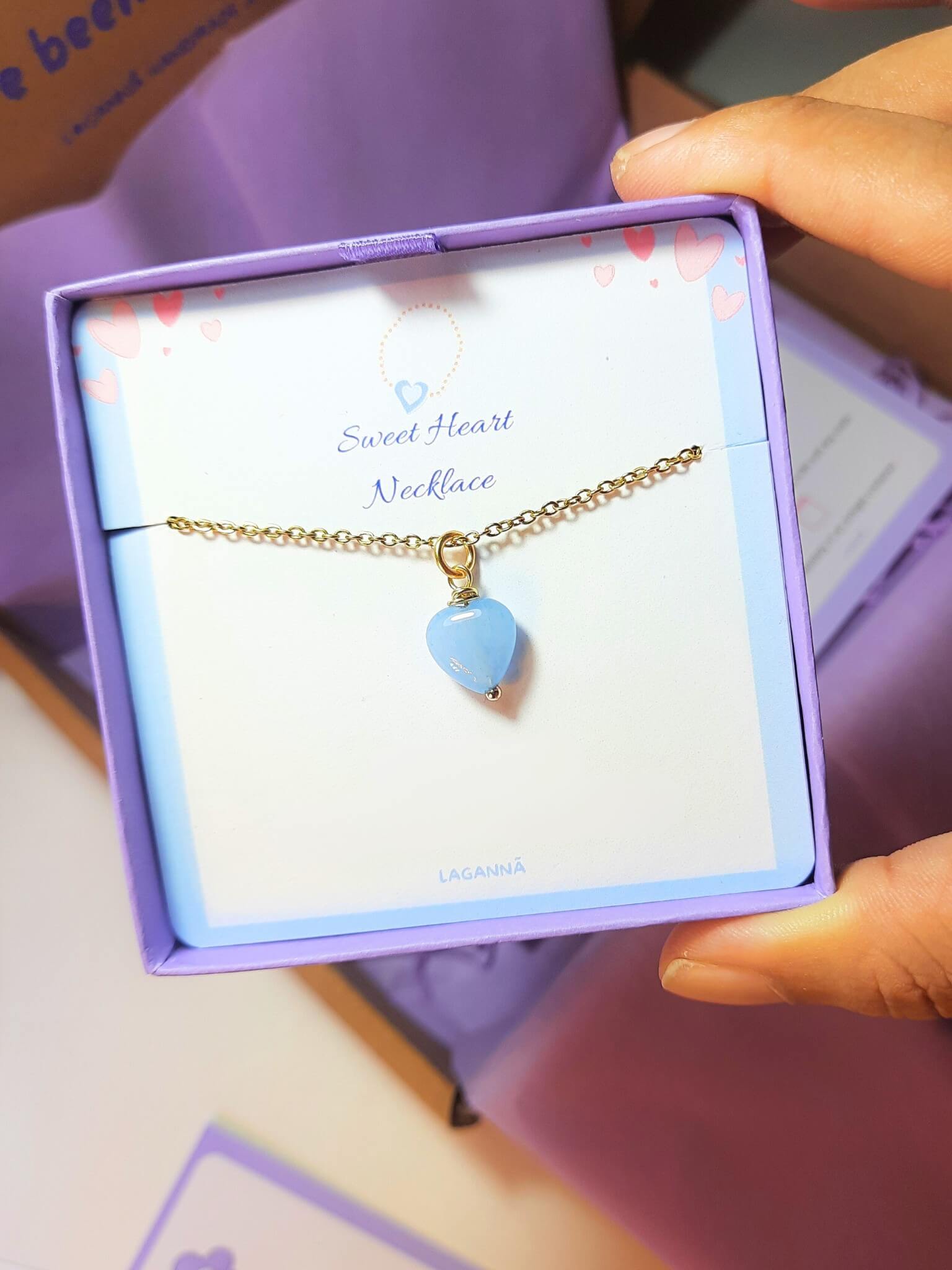 Sweet heart blue chalcedony necklace jewelry box held in hand showing handmade gold wire wrapped healing crystal gift set, Sri Lankan artisan throat chakra pendant featuring natural heart-shaped blue gemstone perfect as communication jewelry gift for calm and emotional healing with elegant presentation