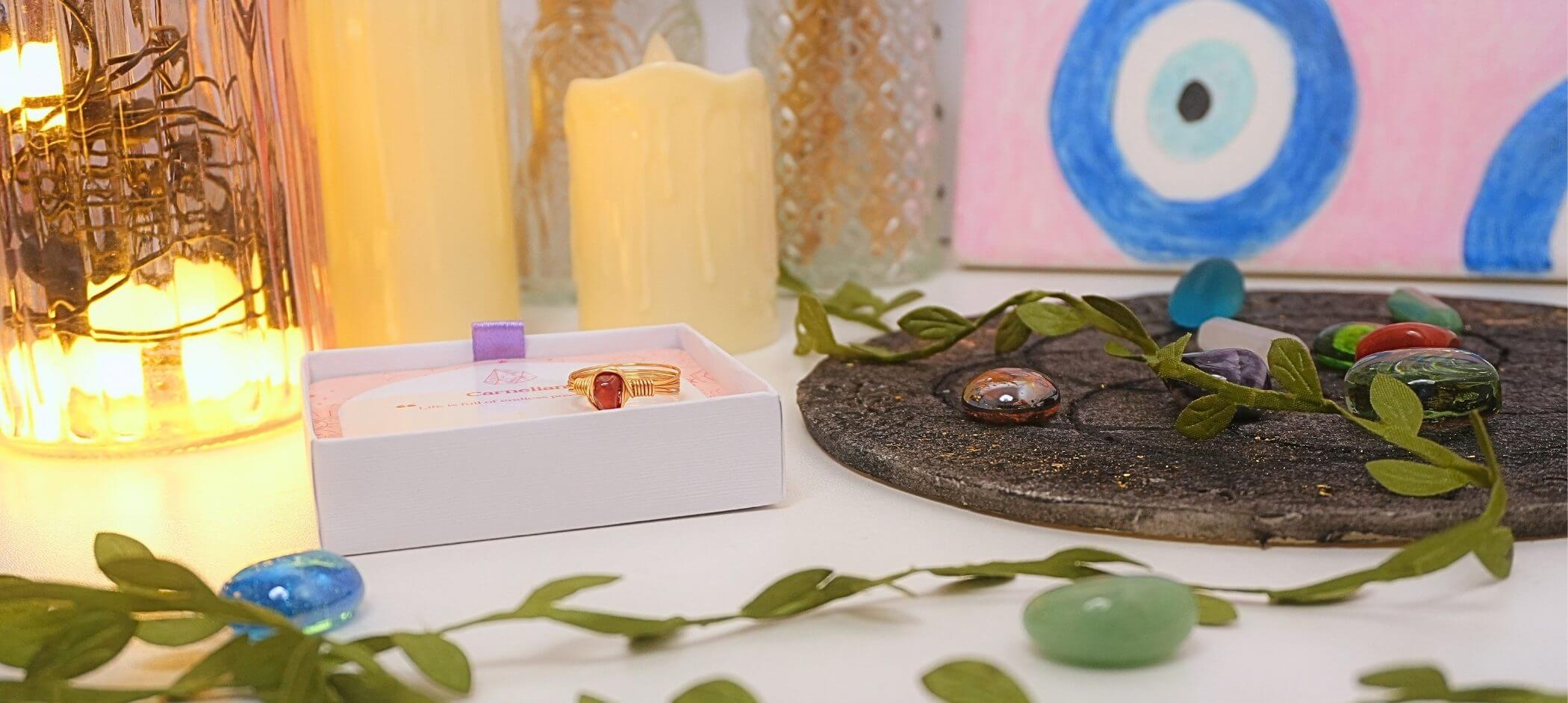 Carnelian gold wire wrapped ring in Laganna gift box surrounded by candles crystals and evil eye art – wisdom and guidance healing crystal jewelry blog banner, Laganna Sri Lanka
